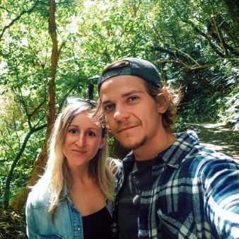 Sabina and Liam smiling at the camera in lush forest