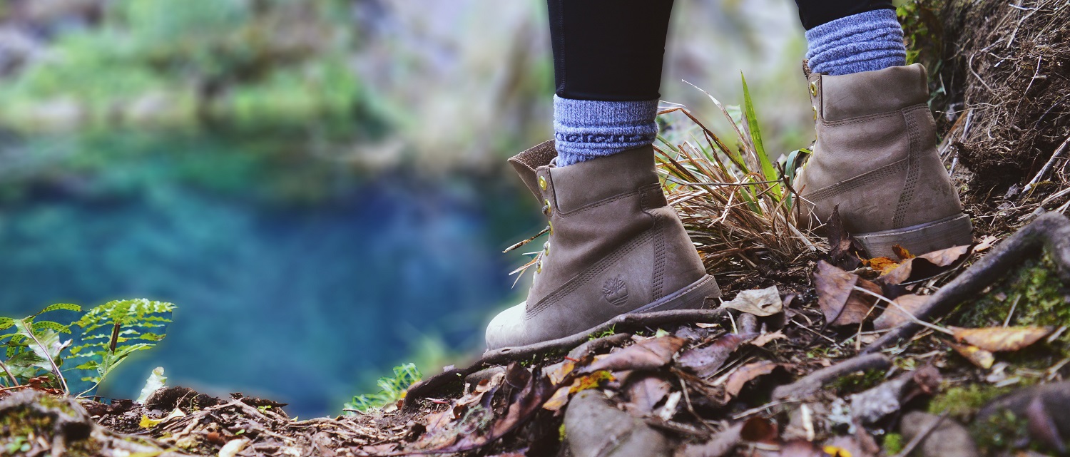 Close up of hiker’s boots at the edge of a clear icy-blue lagoon near Kuratau, North Island, New Zealand.