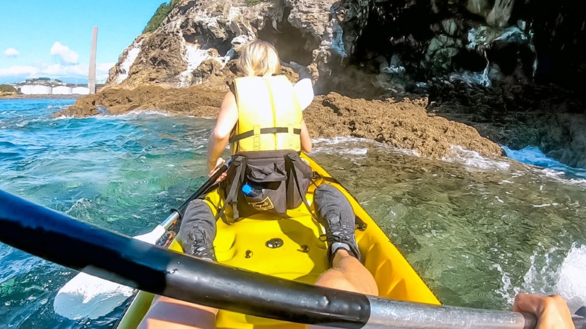 Sabina paddling towards the rugged rocks of Sugar Loaf Island near New Plymouth coast, North Island, New Zealand