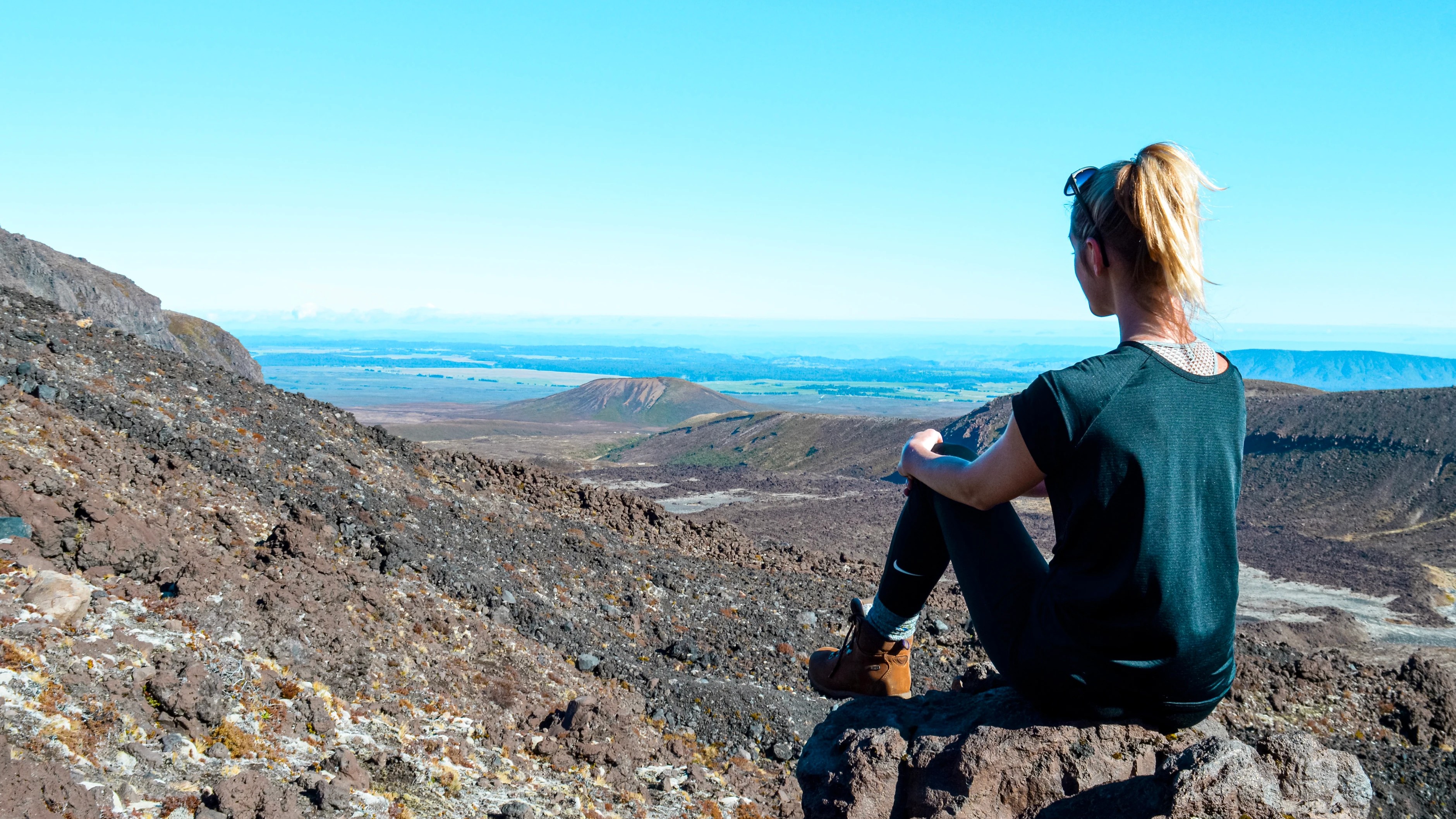 Sabina sitting on volcanic lava rocks after climbing the challenging Devils’ Staircase admiring the views of the vast landscape of the Central Plateau, North Island, New Zealand.