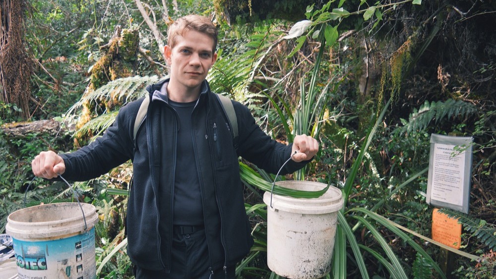 Liam carrying buckets of gravel to help maintain a forest walking track near National Park Village, North Island, New Zealand.