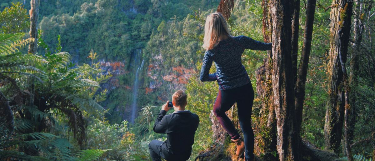 Couple of hikers looking at Tupapakurua Falls from a viewpoint along a hiking trail through lush native forest, North Island, New Zealand.