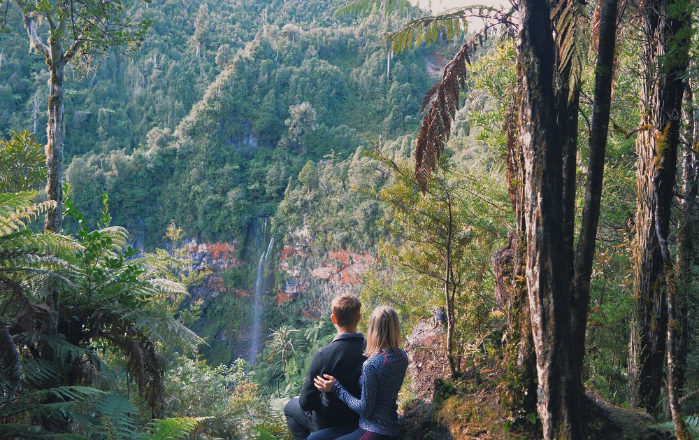 First glimpse of Tupapakurua Waterfall flowing down a red rockface covered by native greenery of this part of the Ruapehu region, New Zealand.